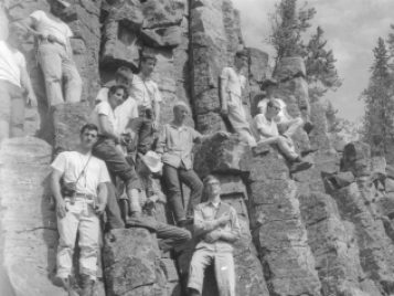 A black-and-white photograph of nine male students reclining against rock face.